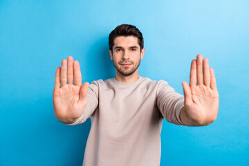 Poster - Photo of serious man with stylish haircut dressed beige sweatshirt stretching palms to you showing stop isolated on blue color background