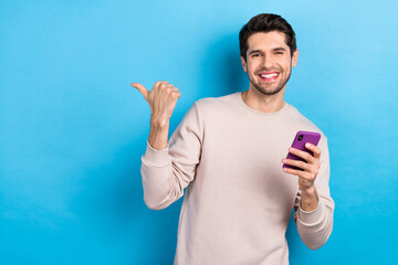 Canvas Print - Portrait of young guy hold smart phone direct finger empty space wear beige sweatshirt isolated on blue color background