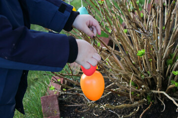 Wall Mural - Close up of a child hanging colorful decorative easter eggs on a small bush