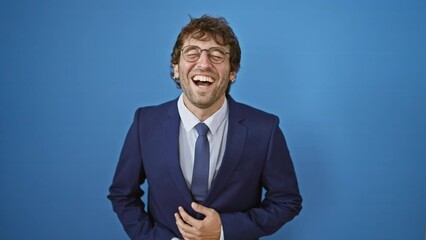 Poster - Joyful young man in a business suit laughs out loud, flashing a bright, handsome smile and clasping his hands in sheer delight! isolated against blue background.