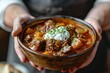 A person garnishing a bowl of Hungarian goulash with sour cream
