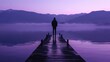 An individual stands on a dock silhouette blending in with the hazy purple mountains in the distance. . .