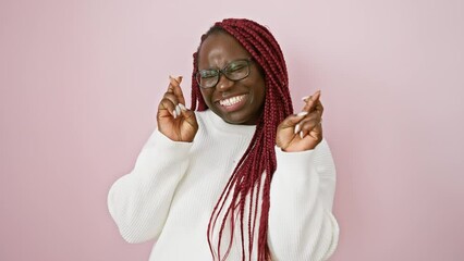 Poster - Happy black woman with braids wearing glasses and white sweater over pink background crossing fingers