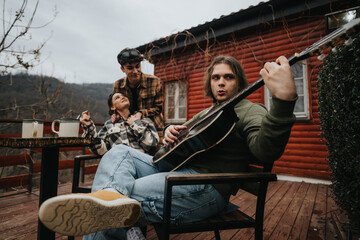 Wall Mural - Young adults relax with guitars and coffee on a wooden porch by a rustic cabin, sharing a moment of music and laughter.