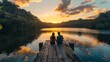 A couple sits side by side on a wooden pier backs to the camera watching the sunset over a calm lake surrounded by lush green . .