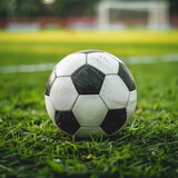 Fototapeta Sport - Soccer ball on a grassy field - Classic black and white soccer ball on lush green grass, in an empty field preparing for a match