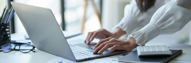 Wall Mural - Asian businesswoman or executive manager using laptop computer is checking data, typing, searching, financial records, statistics, taxes, income in online business in office.