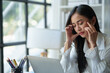 © crizzystudio - Asian businesswoman is tired, headache, sleepy and bored from sitting at a desk for a long time working on a laptop computer. Problematic financial paperwork Office syndrome concept.