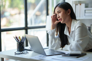 Wall Mural - Asian businesswoman is tired, headache, sleepy and bored from sitting at a desk for a long time working on a laptop computer. Problematic financial paperwork Office syndrome concept.