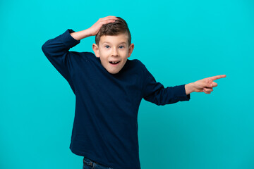 Wall Mural - Little kid boy isolated on blue background surprised and pointing finger to the side