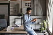 © fizkes - Serious young Indian office worker man typing message on smartphone, leaning at workplace, using mobile phone for online communication in modern workspace interior
