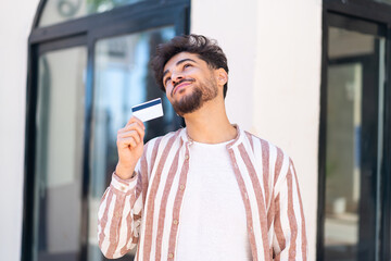 Wall Mural - Handsome Arab man at outdoors holding a credit card and thinking