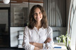 © fizkes - Happy confident young professional woman in white shirt standing in office with arms folded at chest, looking at camera with toothy smile. Attractive female business leader head shot portrait