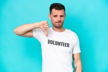 Wall Mural - Young volunteer caucasian man isolated on blue background showing thumb down with negative expression