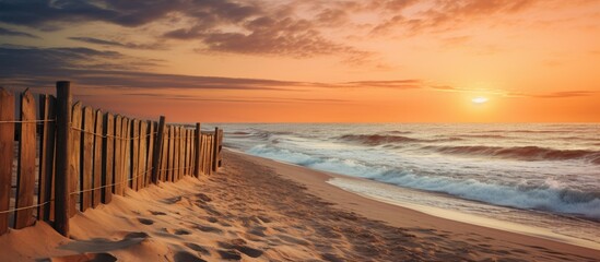 Wall Mural - Wooden fence stretching across the sandy beach, overlooking the tranquil ocean under the warm hues of the sunset