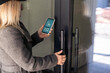 © Angelov - Woman locking smartlock on the entrance door using a smart phone. Concept of using smart electronic locks with keyless access.