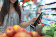 Woman shopping in supermarket looking at shopping list on phone screen with shopping list Compare prices at stores