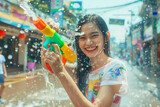 Fototapeta Panele - Happy traveler asian woman wearing summer shirt holding colourful squirt water gun over blur city, Water festival holiday concept