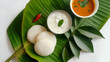 Steamed Idly served on a Banana Leaf with Sambhar and Coconut Chutney, styled with curry leaves on a white background