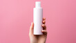 hand holding a white bottle on the solid pink background