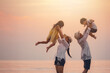 © Garun Studios - beach, children, childhood, sea, silhouette, together, friendship, parent, freedom, relax. A family is playing on the beach, with a woman holding a child in her arms and another child being lifted.