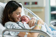 © Tjeerd - Cheerful new mother carrying and smiling to her newborn baby while resting on the hospital bed after giving birth