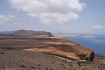 Wall Mural - Views of Caleta de Famara from the viewpoint of El Rio. Turquoise ocean. Blue sky with big white clouds. Caleta de Sebo. Village. Volcanoes. Lanzarote, Canary Islands, Spain