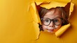 with glasses image featuring a charming with glasses lettle childre peeking through a carefull torn opening in a rich yellow paper backdrop