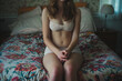 anonymous young woman sitting on bed wearing white underwear, hands clasped concpt of mental health, pregnancy, body issues