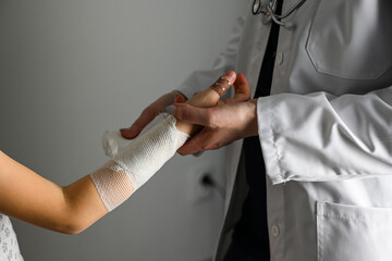 a doctor in a white coat with a stethoscope bandages the hand of a little girl