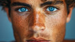 Close-up of a young man with striking blue eyes and freckles, intense gaze, and natural lighting.