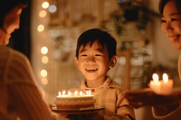 A young child beams with excitement as he's presented a birthday cake with lit candles, family around him