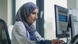 Female doctor in hijab reviewing medical record at computer in clinic