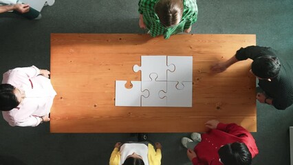 Wall Mural - Top view of business man gathering last piece of jigsaw to complete puzzle. Group of diverse team working together to solve the puzzle while putting hands together and clapping hands. Convocation.