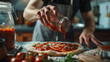 A man's hands make a pizza and pour red tomato sauce from a glass jar