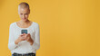 Young hairless woman, texting, communicating on social networks, mobile phone, advertising space, isolated on yellow background in studio