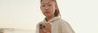 © Andrii Nekrasov - Close up, asian girl in sportswear uses the phone while standing on the embankment in the morning, Panorama
