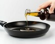 Pouring oil from bottle into frying pan on white background, closeup