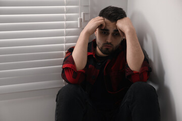 Wall Mural - Sad young man near closed blinds at home