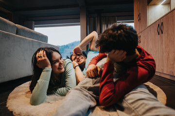 Wall Mural - A group of cheerful young adults enjoying a playful and happy moment while sitting on a soft rug inside a modern home.