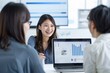 © Huong - Three Japanese office workers are smiling and discussing work in the meeting room, with a laptop displaying financial data on the screen