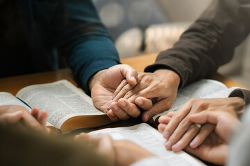Wall Mural - Group of young Christians praying, holding hands and praying together The concept of praying to God in the home as a team Pray to God with the Bible for forgiveness and faith.