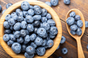 Wall Mural - Ripe blueberries in a wooden bowl and spoon on a background of scattered berries. Concept of healthy and dieting eating.