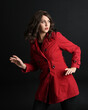 close up portrait of beautiful brunette woman model, wearing red trench coat jacket.
isolated on dark studio background with shadows. hand gesture reaching out