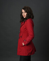 Wall Mural - close up portrait of beautiful brunette woman model, wearing red trench coat jacket. isolated on dark studio background with shadows.  back view, facing away from camera.