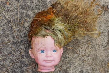 Wall Mural - plastic head with face and dirty hair of a girl's toy children's doll lies on the ground during the day on the street