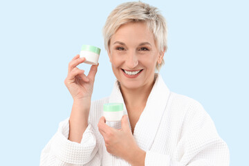 Sticker - Mature woman with jars of cream on blue background, closeup