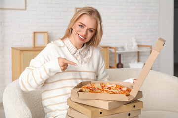 Canvas Print - Young woman pointing at boxes with tasty pizza at home