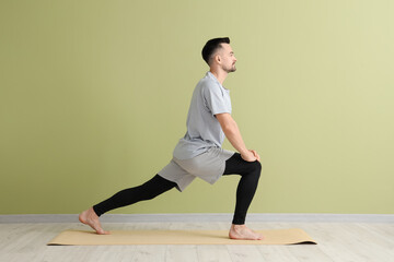 Canvas Print - Handsome man doing yoga on mat near green wall