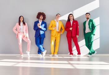 Group of positive young people in colorful business suits standing against a gray wall. They represent diversity and teamwork, smiling happily in this portrait of a dynamic business team.